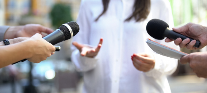 Journalist interview with woman spokesperson surrounded by microphones, representing media relations and PR strategy.