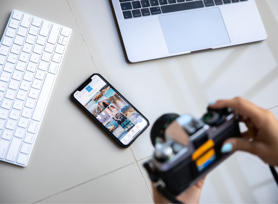 person holding a camera above a keyboard and a phone showing an instagram feed