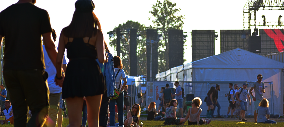 Outdoor festival scene with people walking and sitting on the grass near event tents and staging representing a brand activation setting