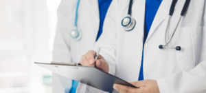 Two medical professionals wearing white coats and stethoscopes review notes on a clipboard.