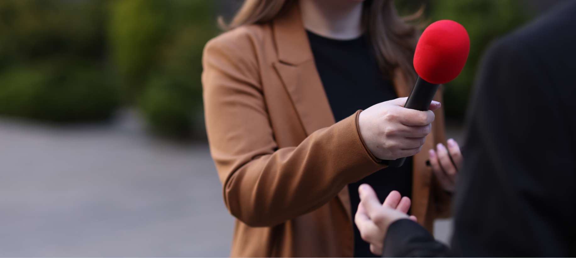 Reporter holding a red microphone while interviewing a person outdoors.