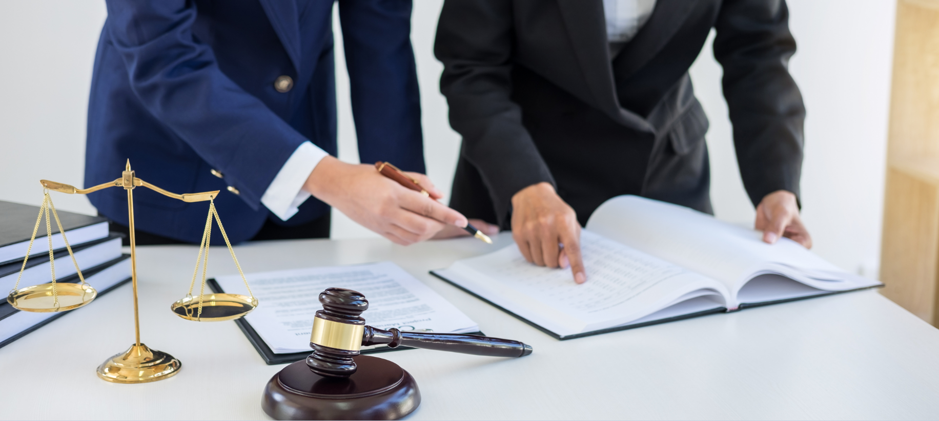Two legal professionals reviewing documents at a desk with scales of justice and a gavel.
